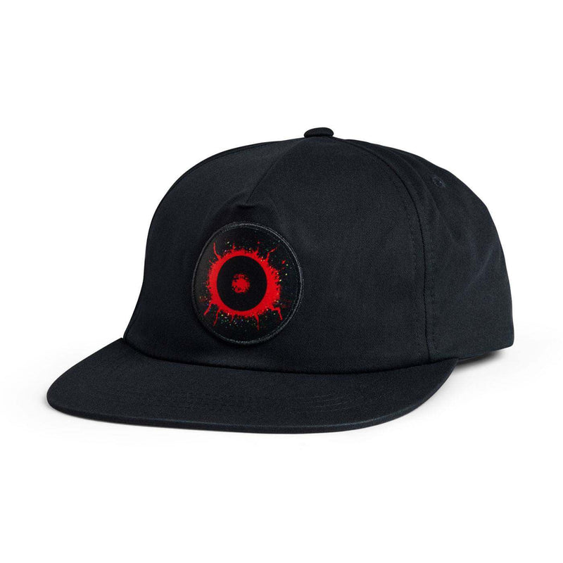 A black flat-brim baseball cap featuring a circular embroidered patch on the front with a red eye design.