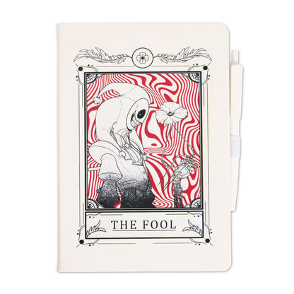 White journal with attached white pen featuring a tarot-style illustration titled “The Fool,” showing The Prototype holding a flower against a red swirling background.