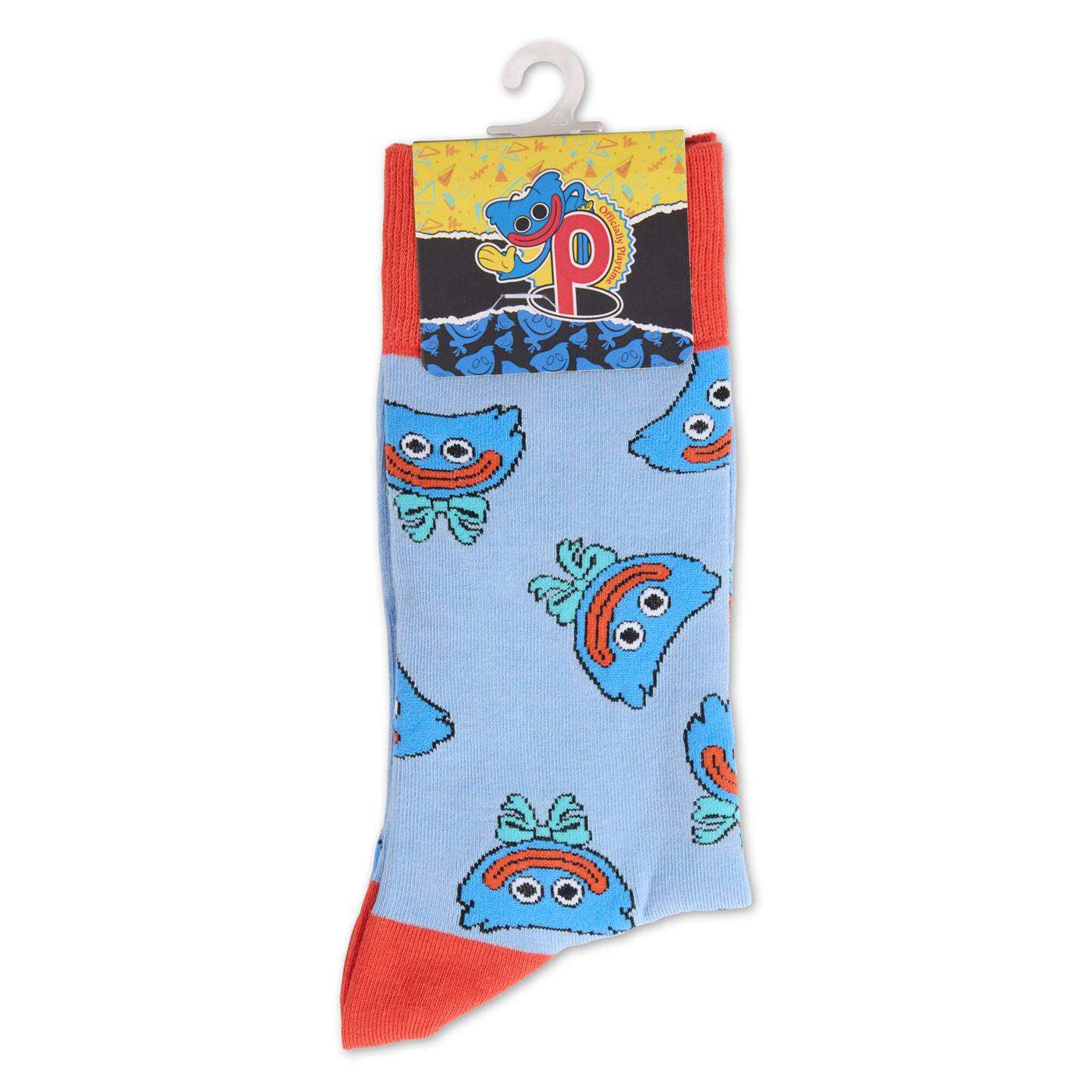 A light blue sock with a repeating pattern of smiling huggy wuggy faces, featuring red toes and heels, hanging from a white plastic hanger.
