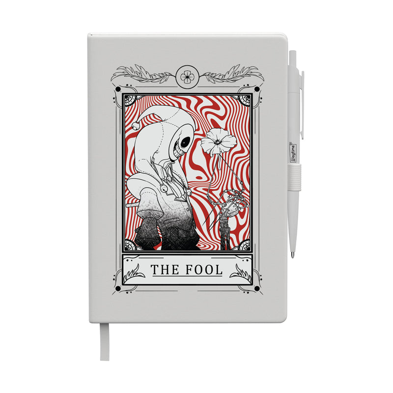 White journal with attached white pen featuring a tarot-style illustration titled “The Fool,” showing The Prototype holding a flower against a red swirling background.